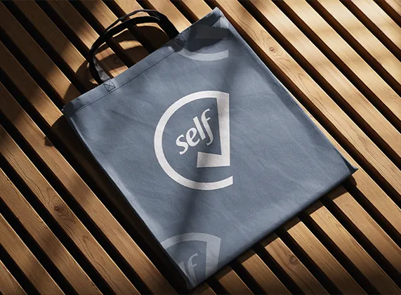 SelfCheck logo on a slate blue tote bag in strong sunlight